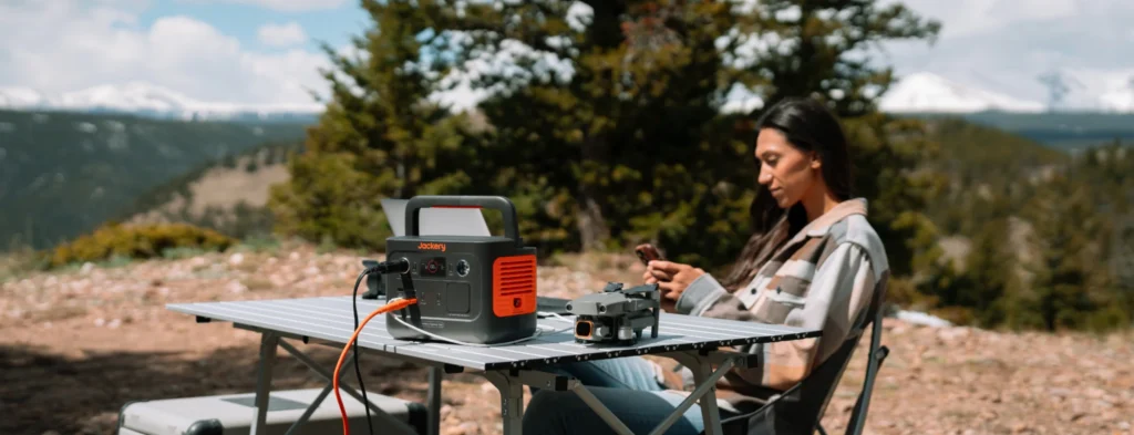 Mujer usando la Jackery 240 v2 para cargar un dron y un portátil en la montaña.