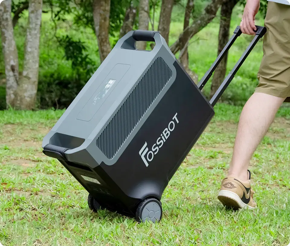 Persona transportando la estación FOSSiBOT F3600 Pro sobre hierba usando sus ruedas y asa telescópica.