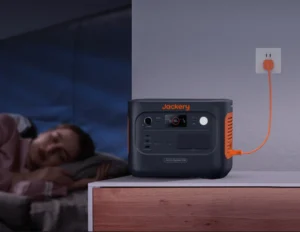 Mujer durmiendo en segundo plano con la estación Jackery Explorer 1000 v2 funcionando silenciosamente en modo UPS en la mesita de noche.