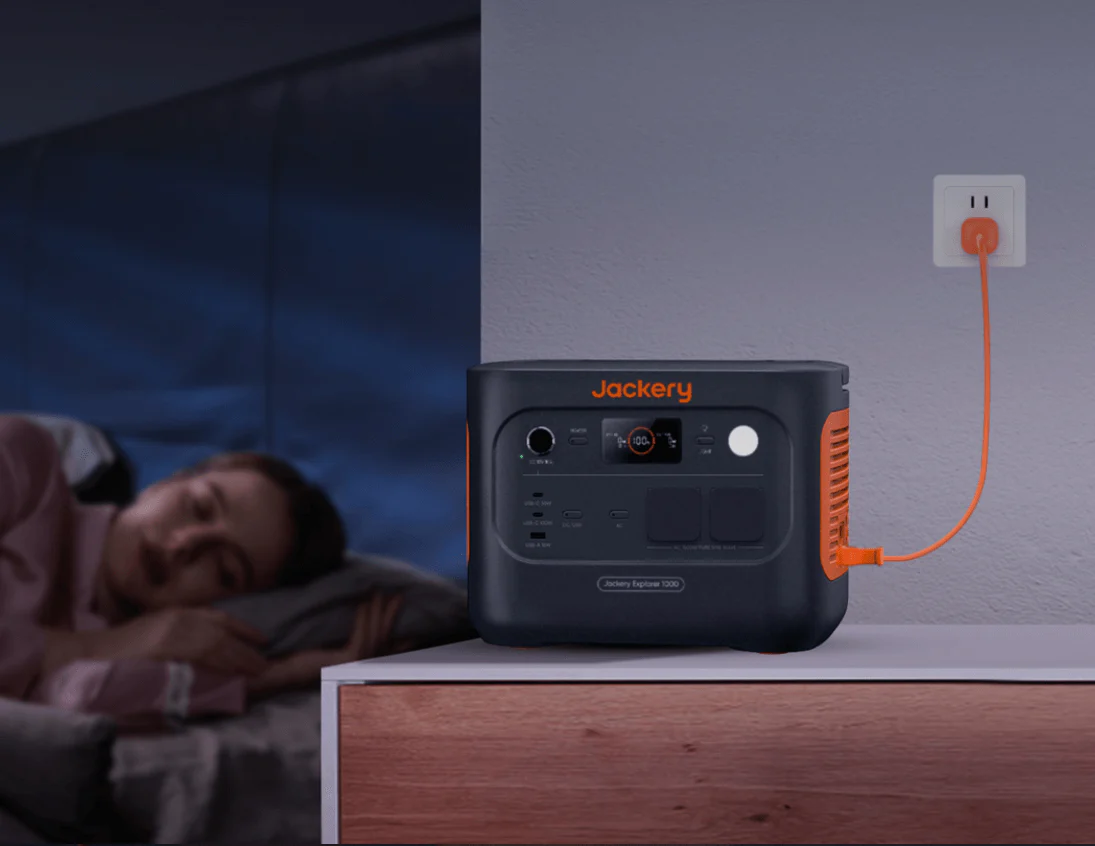 Mujer durmiendo en segundo plano con la estación Jackery Explorer 1000 v2 funcionando silenciosamente en modo UPS en la mesita de noche.