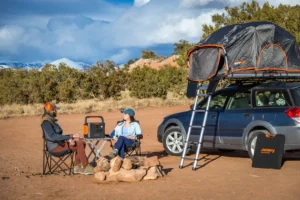 Pareja en un campamento con coche y tienda de techo utilizando la Jackery 1000 v2 para iluminar y cocinar.