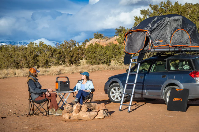 Pareja en un campamento con coche y tienda de techo utilizando la Jackery 1000 v2 para iluminar y cocinar.