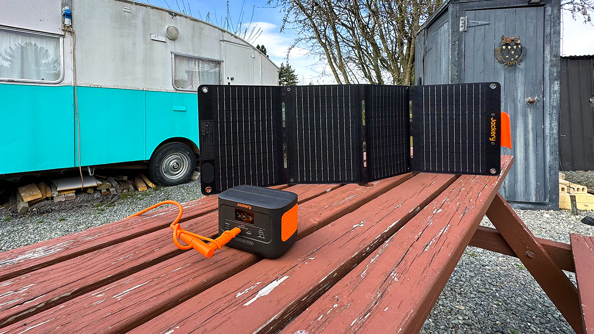 Estación Jackery Explorer 100 Plus conectada a un panel solar plegable SolarSaga en una mesa de madera.