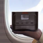 Mano sosteniendo una Jackery Explorer 100 Plus frente a la ventanilla de un avión en pleno vuelo.
