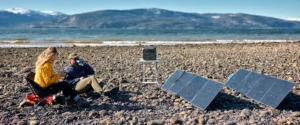 Pareja cargando su Bluetti AC180 con paneles solares plegables en una playa rocosa.